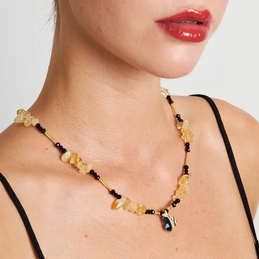 Amber stone necklace featuring raw amber beads, black accents, and a gold-tone blue gemstone pendant, symbolizing natural beauty and healing energy.